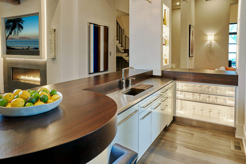 This is an example of a contemporary home bar in Minneapolis with an integrated sink, flat-panel cabinets, white cabinets, wood benchtops and medium hardwood floors.