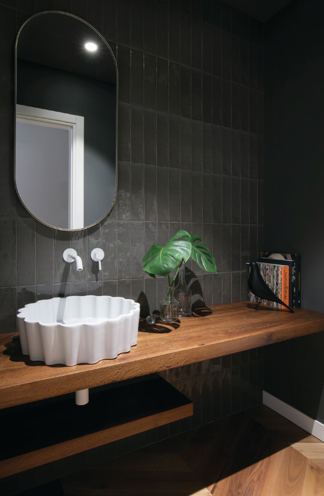 Photo of a mid-sized contemporary powder room in Other with open cabinets, medium wood cabinets, black tile, black walls, a vessel sink, wood benchtops, brown floor, brown benchtops and a floating vanity.