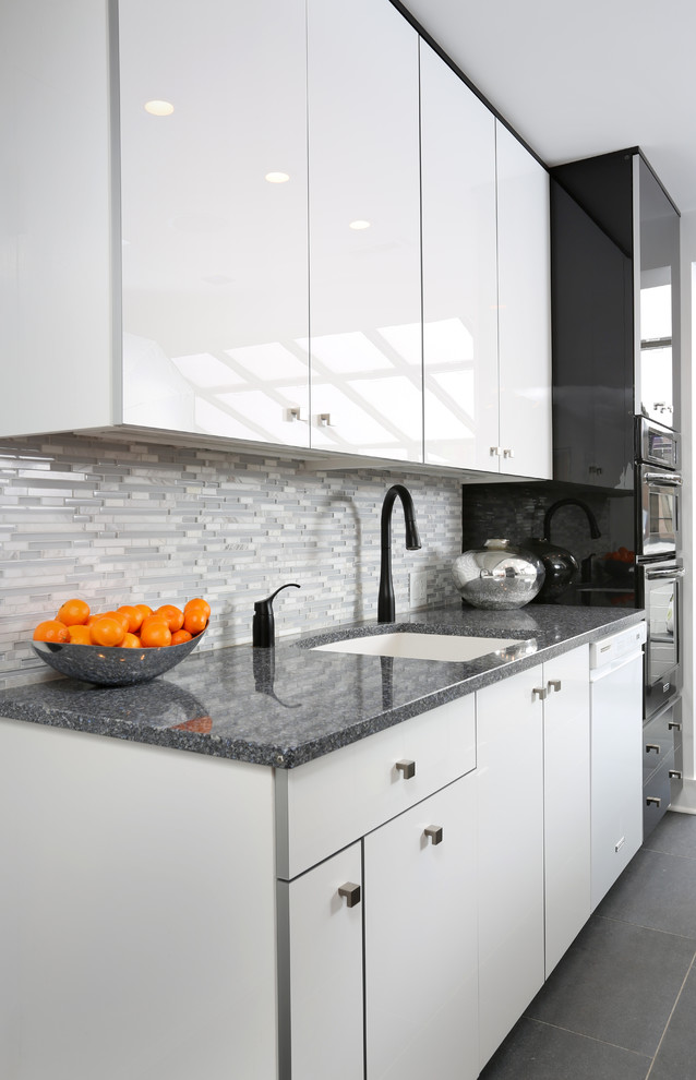 This is an example of a small contemporary galley separate kitchen in Chicago with a single-bowl sink, flat-panel cabinets, white cabinets, quartz benchtops, grey splashback, porcelain floors, no island and glass tile splashback.