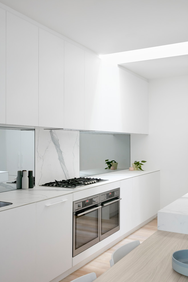 This is an example of a large modern single-wall kitchen in Melbourne with white cabinets, marble splashback, stainless steel appliances, with island, beaded inset cabinets, marble benchtops, white splashback, slate floors, white floor and white benchtop.