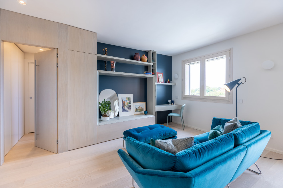 Imagen de sala de estar con biblioteca contemporánea de tamaño medio con paredes azules, suelo de madera clara, televisor colgado en la pared y suelo beige