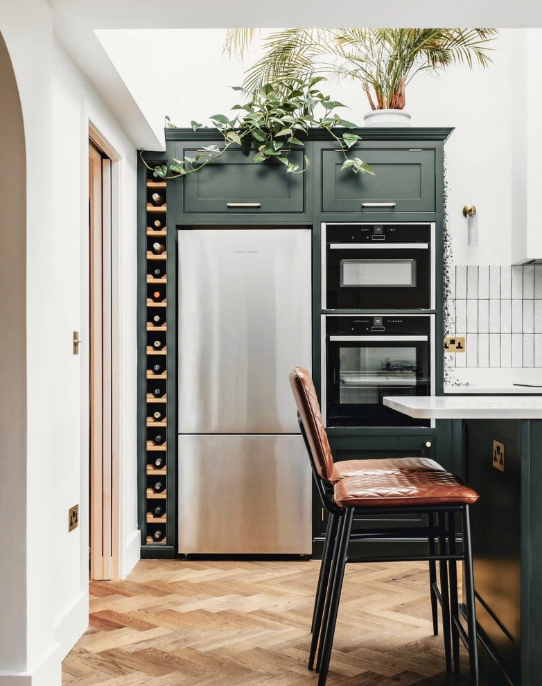 Design ideas for an urban u-shaped kitchen/diner with shaker cabinets, green cabinets, quartz worktops, white splashback, porcelain splashback, stainless steel appliances, medium hardwood flooring, a breakfast bar and white worktops.