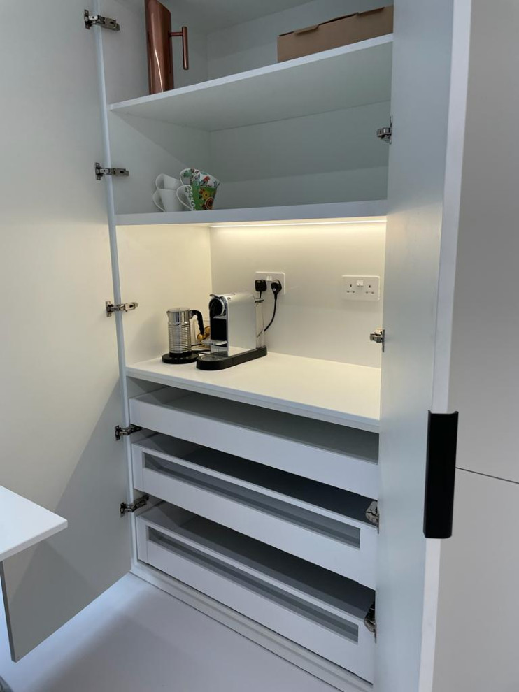 Photo of a small contemporary u-shaped open plan kitchen in London with beaded cabinets, white cabinets, quartz worktops, white splashback, black appliances, white floors, white worktops, a coffered ceiling and feature lighting.