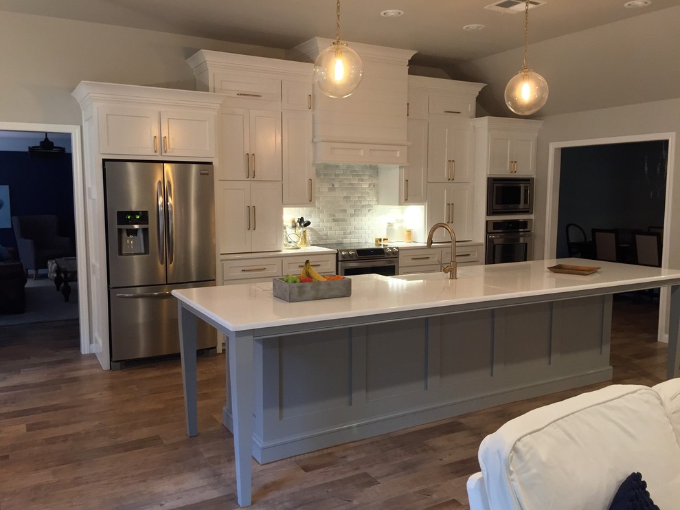 Inspiration for a mid-sized transitional single-wall open plan kitchen in Dallas with a farmhouse sink, shaker cabinets, white cabinets, quartzite benchtops, grey splashback, stone tile splashback, stainless steel appliances, medium hardwood floors and with island.