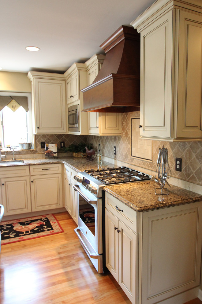 Mid-sized country l-shaped kitchen in New York with an undermount sink, raised-panel cabinets, white cabinets, granite benchtops, beige splashback, ceramic splashback, stainless steel appliances, light hardwood floors, with island, beige floor and brown benchtop.