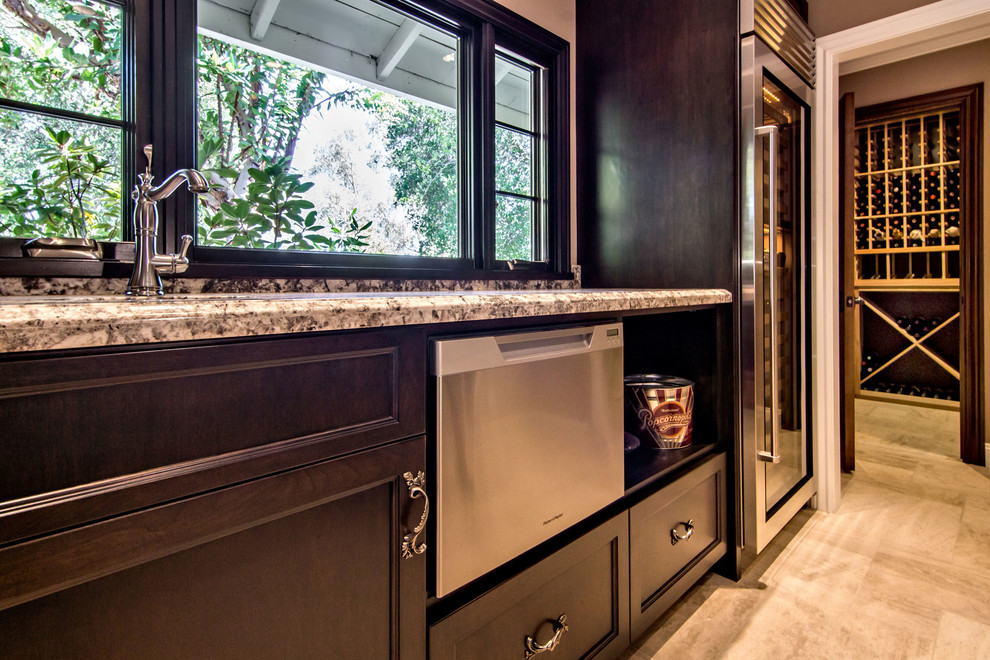 Design ideas for an expansive traditional galley wet bar in San Francisco with an undermount sink, beaded inset cabinets, brown cabinets, granite benchtops, grey splashback, stone slab splashback, limestone floors, beige floor and grey benchtop.