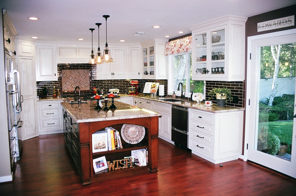 This is an example of a mid-sized transitional u-shaped eat-in kitchen in Los Angeles with an undermount sink, raised-panel cabinets, white cabinets, granite benchtops, black splashback, subway tile splashback, stainless steel appliances, medium hardwood floors, with island and brown floor.