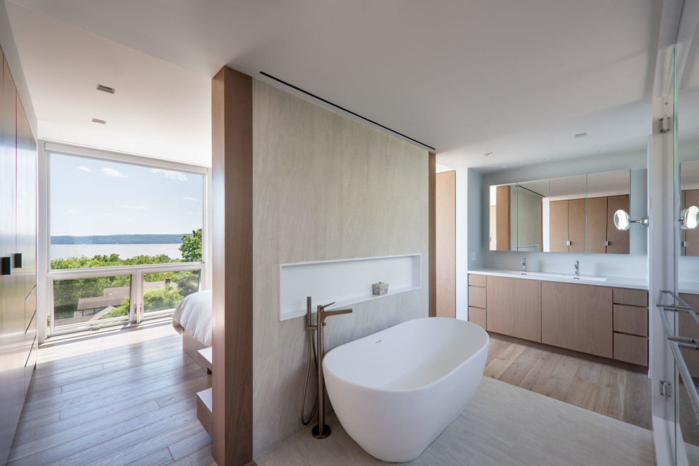 Photo of a contemporary master bathroom in New York with flat-panel cabinets, light wood cabinets, a freestanding tub, beige walls, a trough sink, beige floor and white benchtops.