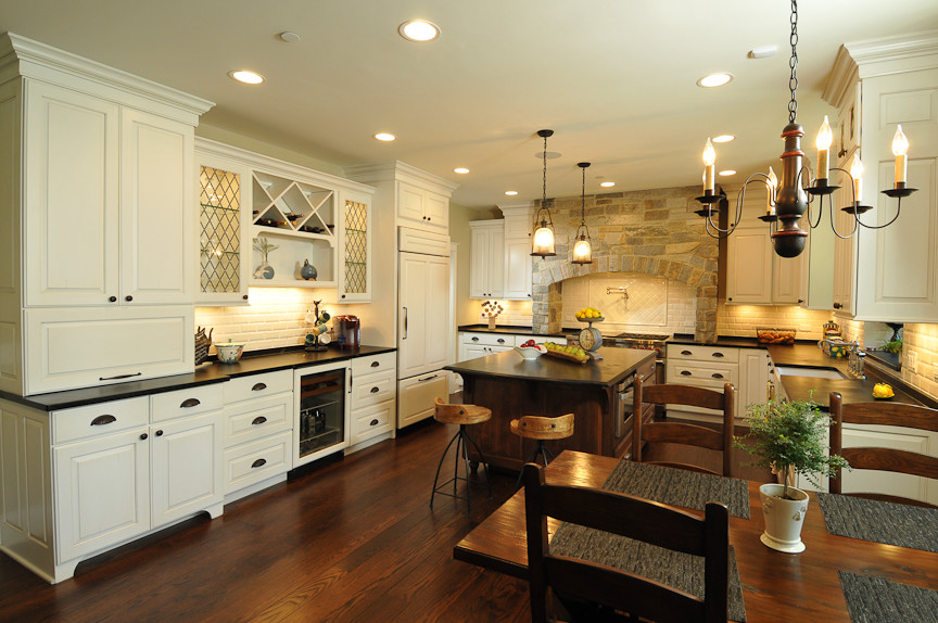 Example of a mountain style l-shaped eat-in kitchen design in Chicago with a farmhouse sink, raised-panel cabinets, white cabinets, soapstone countertops, white backsplash, subway tile backsplash and paneled appliances