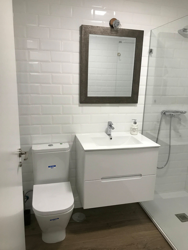 This is an example of a small contemporary 3/4 bathroom in Madrid with an alcove shower, a two-piece toilet, white tile, ceramic tile, white walls, laminate floors, a wall-mount sink, engineered quartz benchtops, brown floor, a sliding shower screen and white benchtops.
