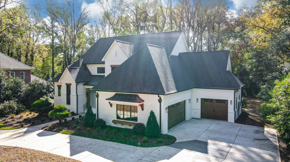 Foto della villa grande bianca country a due piani con rivestimento in mattone verniciato, tetto a capanna, copertura a scandole, tetto nero e pannelli e listelle di legno