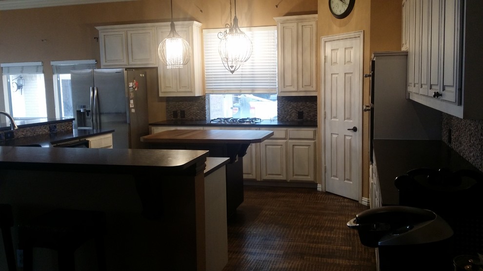 Example of a large transitional brown floor open concept kitchen design in Dallas with an undermount sink, raised-panel cabinets, white cabinets, granite countertops, gray backsplash, stone tile backsplash, stainless steel appliances and an island
