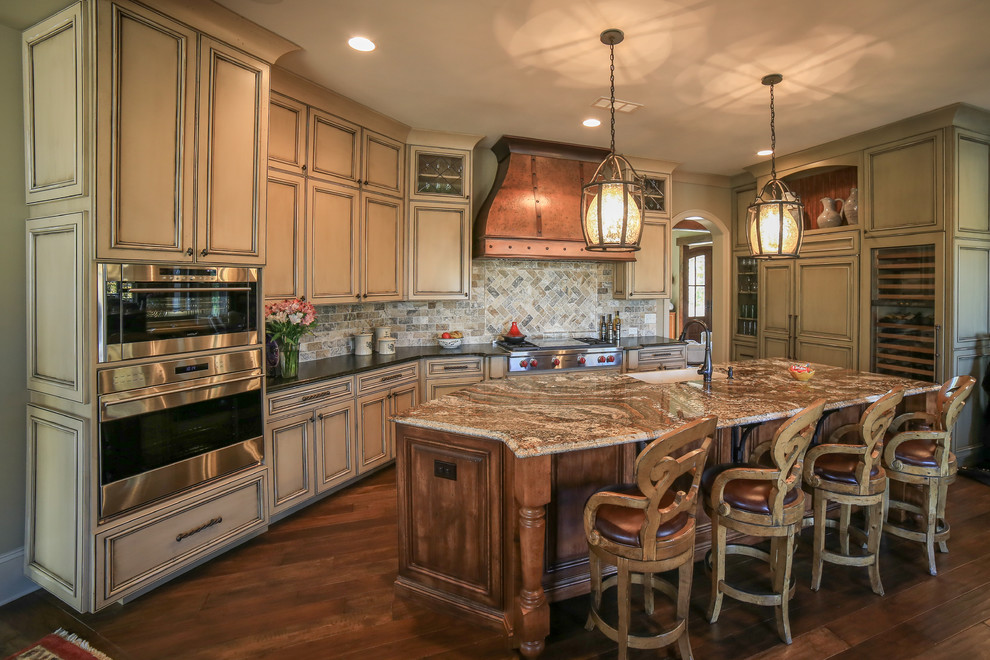 Photo of a large country l-shaped eat-in kitchen in Charlotte with a farmhouse sink, granite benchtops, multi-coloured splashback, stone tile splashback, panelled appliances, dark hardwood floors, with island, flat-panel cabinets and beige cabinets.
