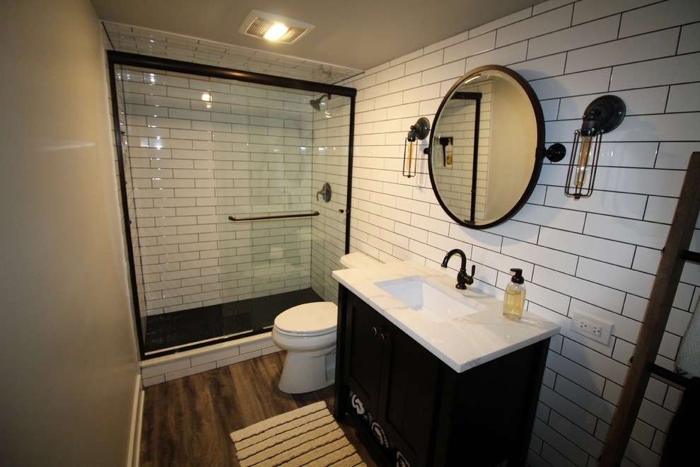 Design ideas for a mid-sized industrial 3/4 bathroom in Nashville with black cabinets, an alcove shower, a two-piece toilet, white tile, subway tile, grey walls, dark hardwood floors, an undermount sink, marble benchtops, brown floor, a sliding shower screen and white benchtops.