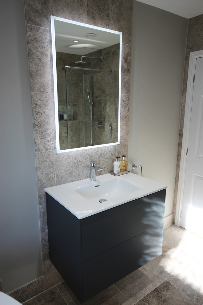This is an example of a large contemporary master wet room bathroom in Surrey with flat-panel cabinets, grey cabinets, a freestanding tub, a wall-mount toilet, gray tile, stone tile, grey walls, limestone floors, a wall-mount sink and grey floor.
