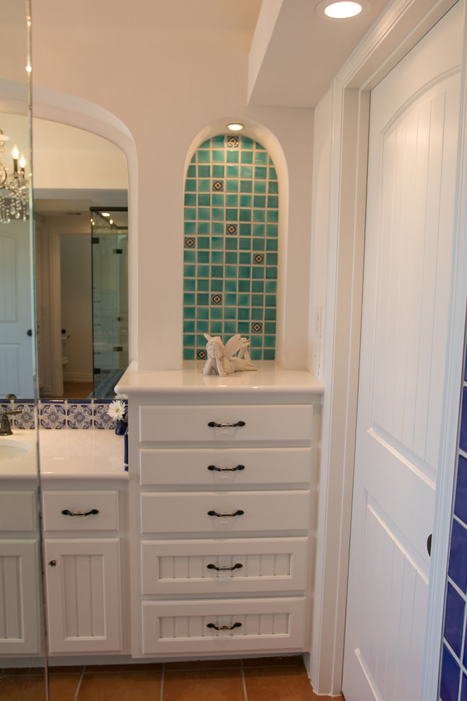 This is an example of a mid-sized mediterranean master bathroom in Austin with recessed-panel cabinets, white cabinets, a corner shower, blue tile, multi-coloured tile, ceramic tile, white walls, terra-cotta floors, an undermount sink, brown floor, a shower curtain and white benchtops.