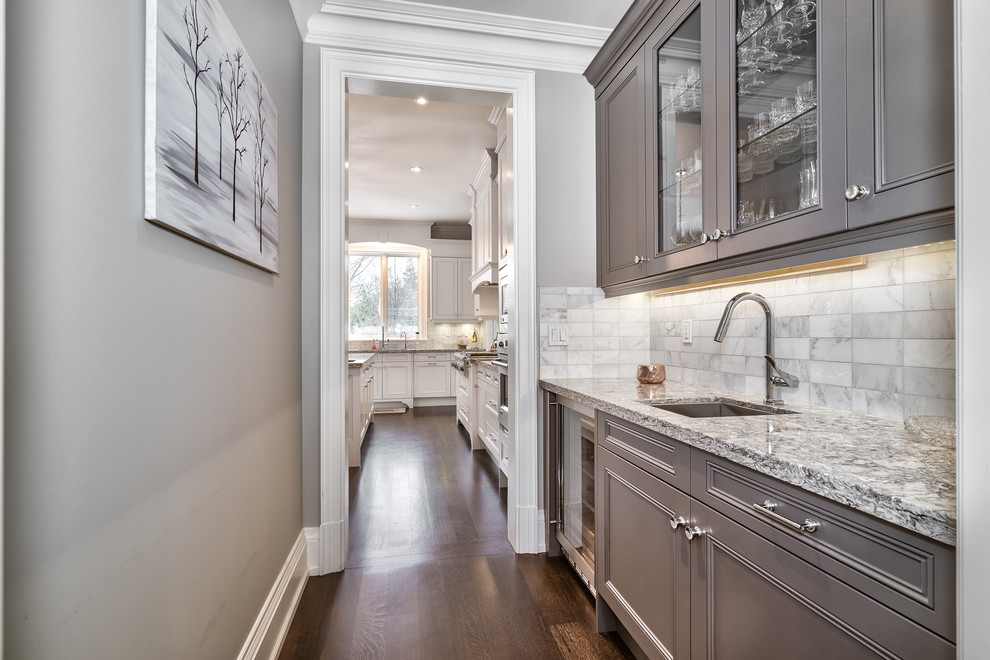 This is an example of a mid-sized transitional single-wall wet bar in Toronto with an undermount sink, beaded inset cabinets, grey cabinets, granite benchtops, grey splashback, marble splashback, dark hardwood floors, brown floor and multi-coloured benchtop.