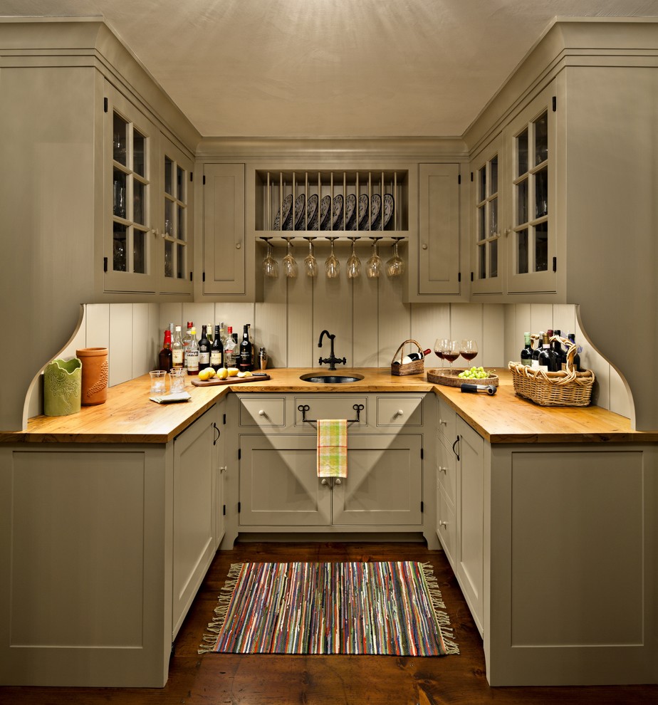 Photo of a country u-shaped home bar in New York with grey cabinets, wood benchtops, grey splashback, medium hardwood floors, an undermount sink, glass-front cabinets, brown floor and brown benchtop.