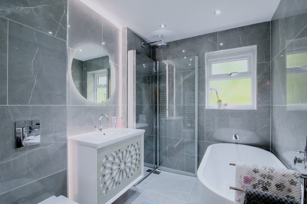 Inspiration for a mid-sized contemporary master wet room bathroom in Manchester with light wood cabinets, a freestanding tub, a wall-mount toilet, gray tile, ceramic tile, grey walls, porcelain floors, a wall-mount sink, grey floor and a hinged shower door.