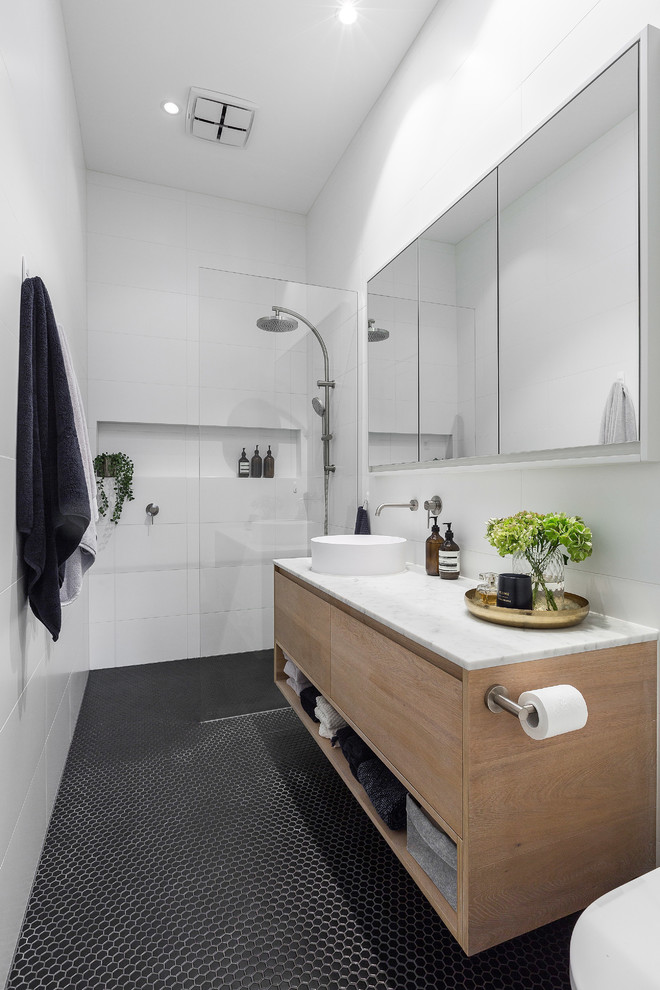 This is an example of a mid-sized contemporary kids wet room bathroom in Melbourne with light wood cabinets, white tile, porcelain tile, white walls, mosaic tile floors, marble benchtops, black floor, an open shower and white benchtops.