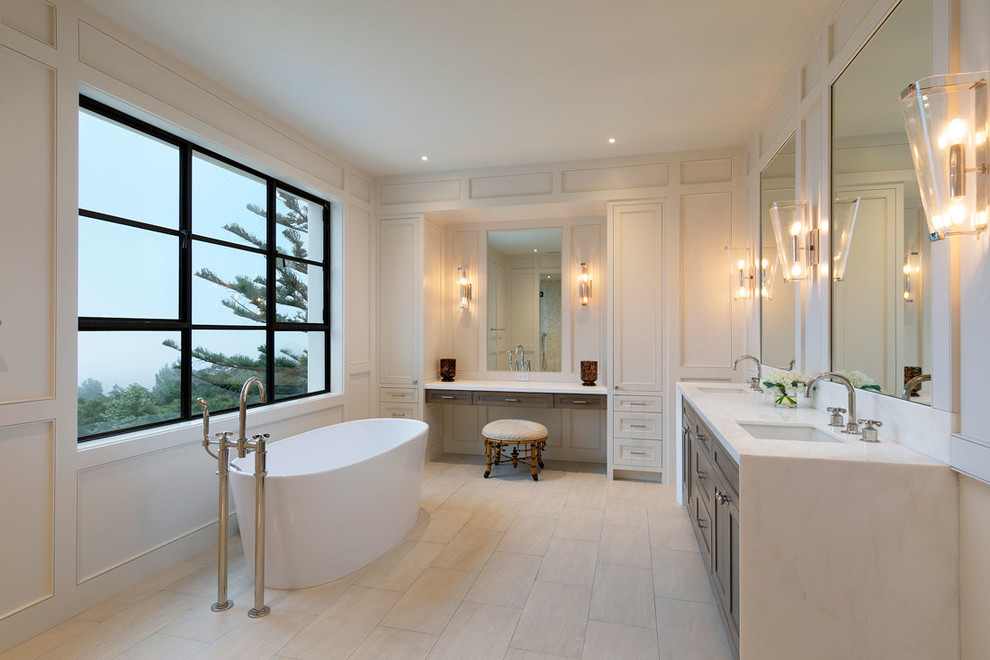 Photo of a mid-sized mediterranean master bathroom in Santa Barbara with furniture-like cabinets, white cabinets, a freestanding tub, white tile, white walls, ceramic floors, an integrated sink, granite benchtops, beige floor and white benchtops.
