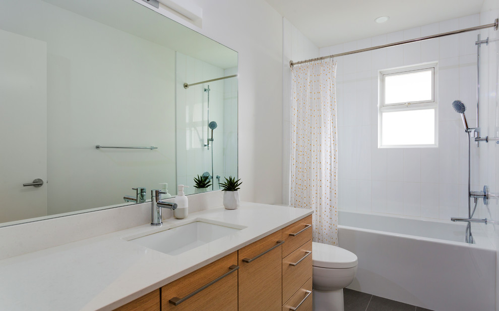 Inspiration for a mid-sized scandinavian kids bathroom in Vancouver with flat-panel cabinets, light wood cabinets, an alcove tub, a shower/bathtub combo, a one-piece toilet, white tile, ceramic tile, white walls, porcelain floors, an undermount sink, engineered quartz benchtops, grey floor and a shower curtain.
