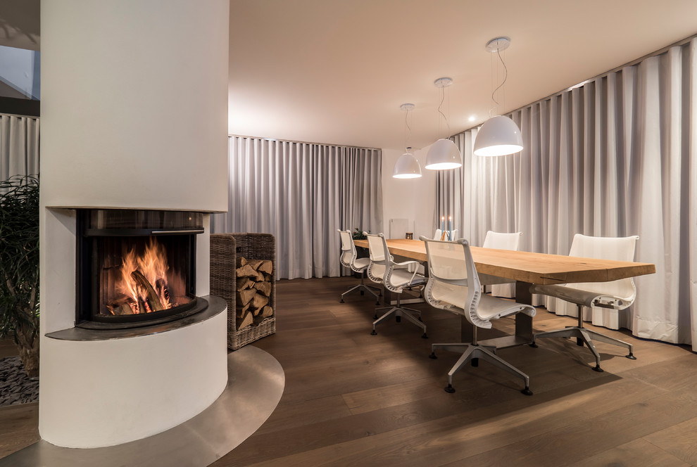 Inspiration for a large contemporary separate dining room in Stuttgart with white walls, medium hardwood floors, a corner fireplace, brown floor and a plaster fireplace surround.