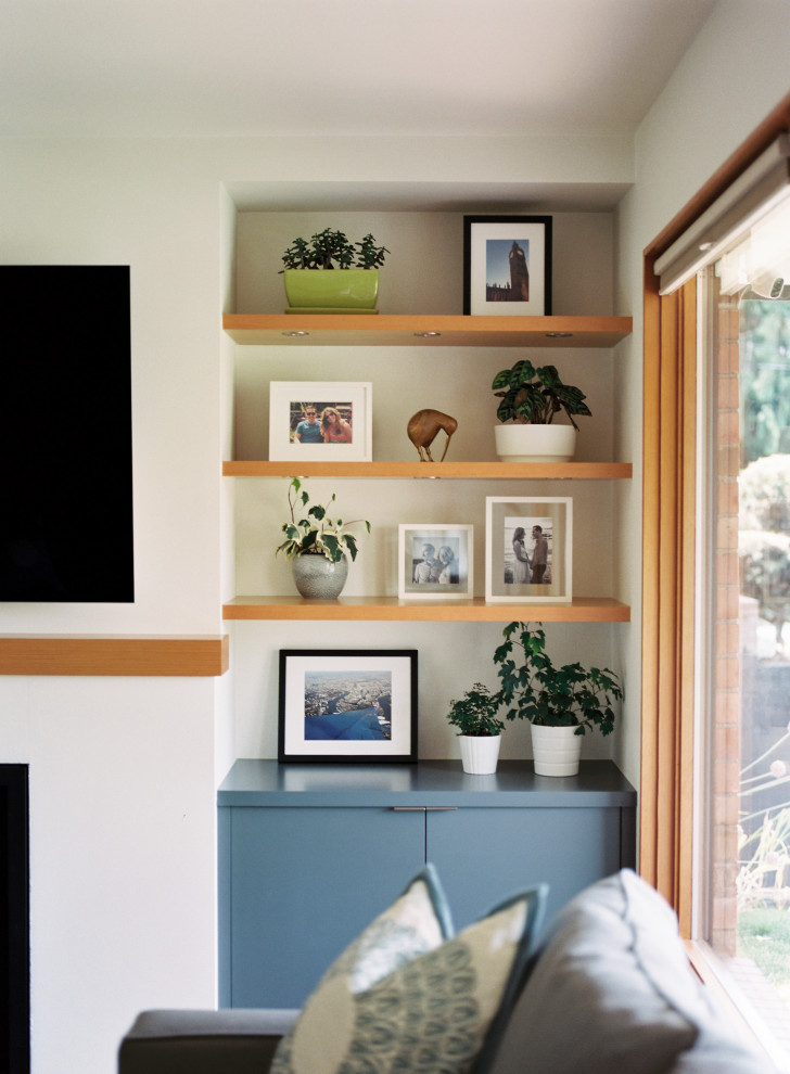 シアトルにある中くらいなミッドセンチュリースタイルのおしゃれなLDK (白い壁、淡色無垢フローリング、標準型暖炉、漆喰の暖炉まわり、壁掛け型テレビ、ベージュの床) の写真