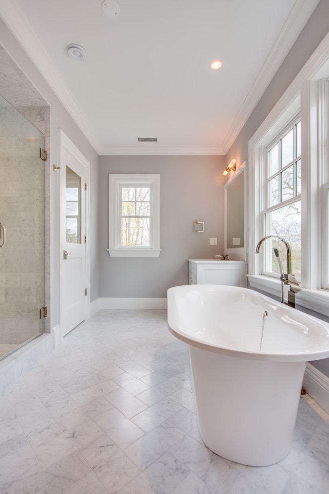 This is an example of a large transitional master bathroom in Other with an undermount sink, recessed-panel cabinets, white cabinets, marble benchtops, a freestanding tub, a corner shower, a one-piece toilet, white tile, stone tile, grey walls, marble floors, white floor and a hinged shower door.