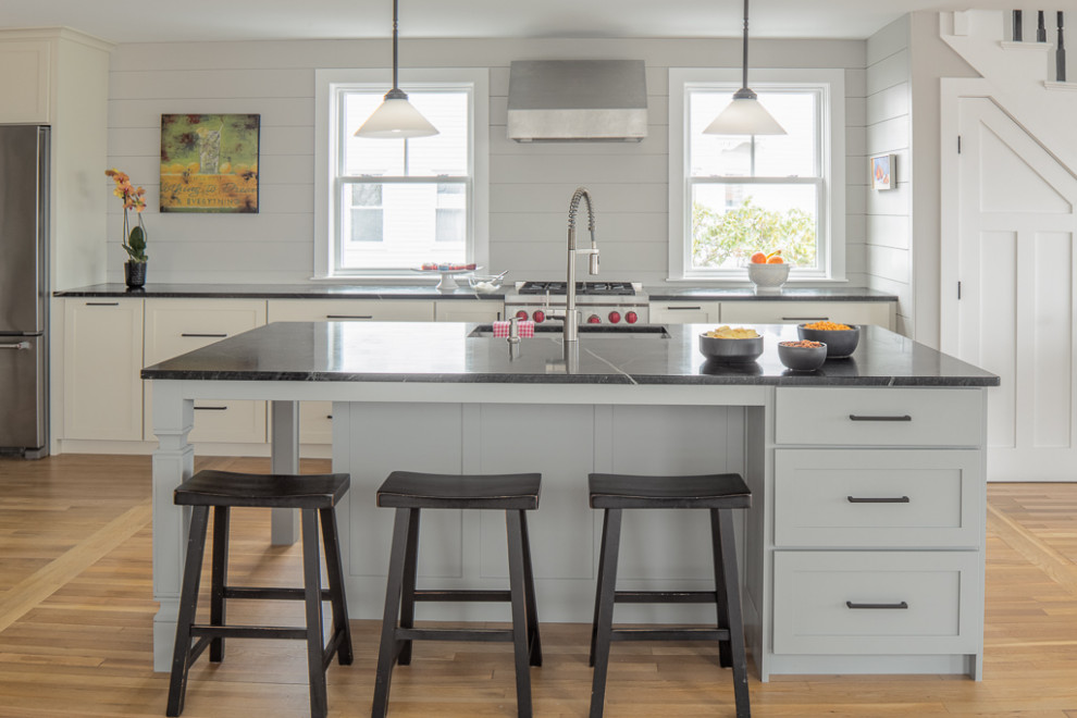 Mid-sized transitional galley kitchen in Portland Maine with an undermount sink, flat-panel cabinets, soapstone benchtops, shiplap splashback, stainless steel appliances, medium hardwood floors, with island and black benchtop.