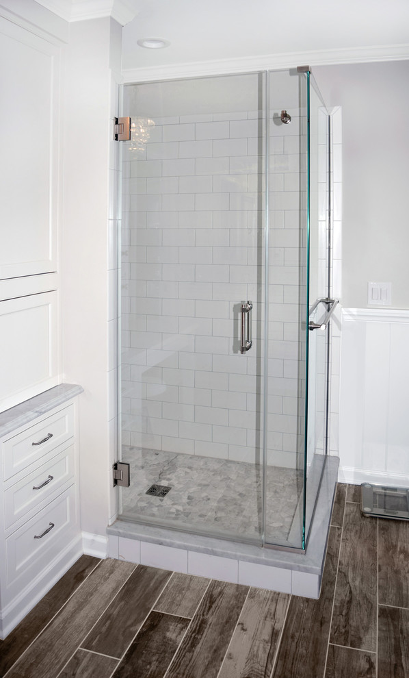 Inspiration for a large traditional master bathroom in Philadelphia with shaker cabinets, white cabinets, a freestanding tub, a one-piece toilet, gray tile, subway tile, grey walls, porcelain floors, an undermount sink, marble benchtops, brown floor and a hinged shower door.