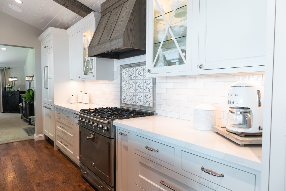 Inspiration for a large single-wall eat-in kitchen in San Francisco with a farmhouse sink, shaker cabinets, white cabinets, quartz benchtops, white splashback, subway tile splashback, stainless steel appliances, medium hardwood floors, with island, brown floor, white benchtop and exposed beam.