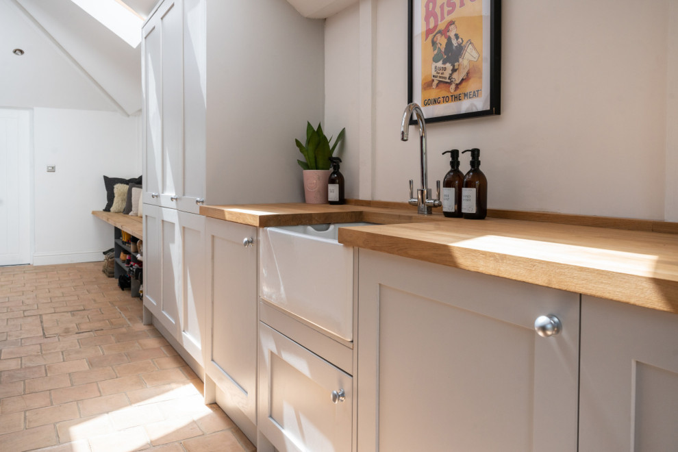 This is an example of a mid-sized contemporary galley utility room in Buckinghamshire with a farmhouse sink, shaker cabinets, grey cabinets, wood benchtops, white walls, vinyl floors, a concealed washer and dryer and yellow benchtop.