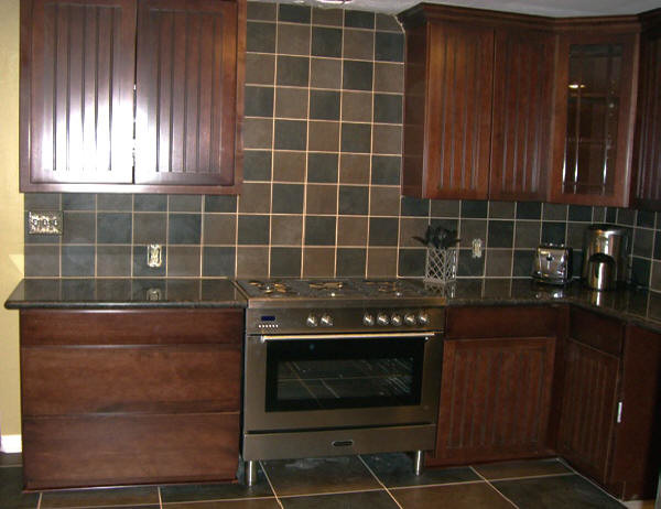 Eat-in kitchen - large transitional u-shaped brown floor and ceramic tile eat-in kitchen idea in Houston with a double-bowl sink, raised-panel cabinets, dark wood cabinets, granite countertops, brown backsplash, ceramic backsplash, stainless steel appliances and no island