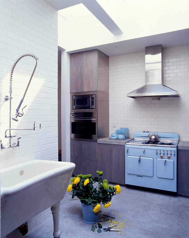 Photo of a mid-sized midcentury l-shaped separate kitchen in New York with a farmhouse sink, flat-panel cabinets, dark wood cabinets, granite benchtops, white splashback, subway tile splashback, coloured appliances and concrete floors.