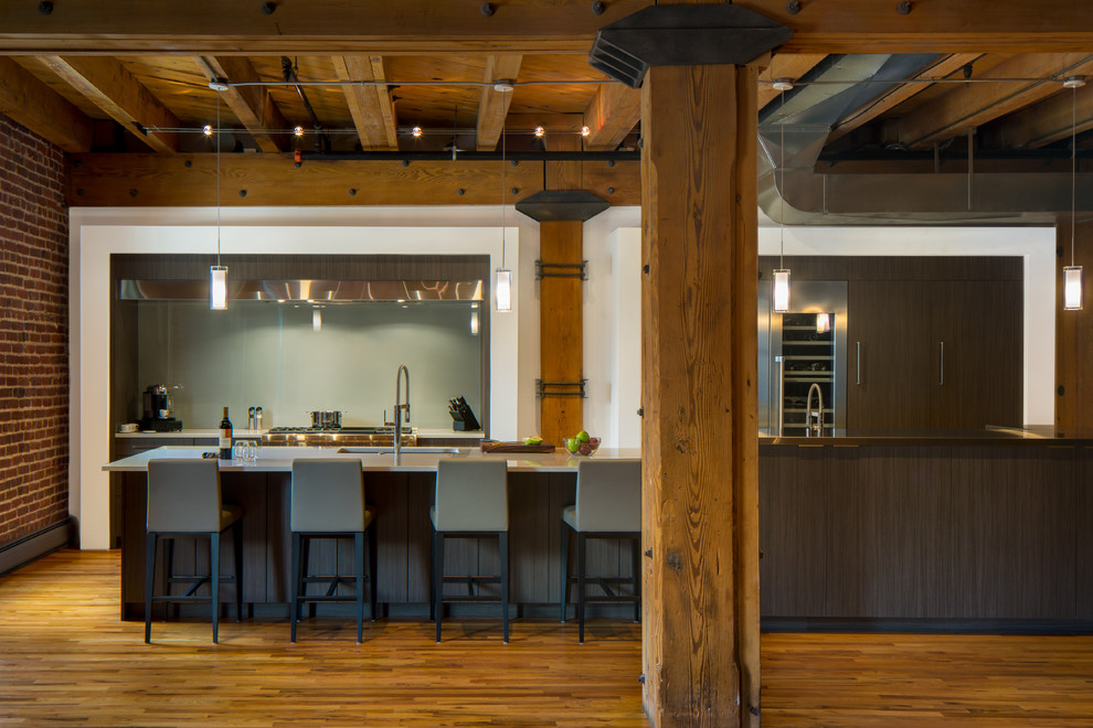 This is an example of an industrial galley kitchen in Denver with an undermount sink, flat-panel cabinets, dark wood cabinets, green splashback, glass sheet splashback, stainless steel appliances, medium hardwood floors and with island.