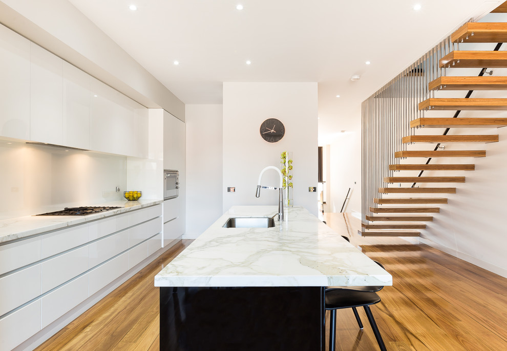 Mid-sized contemporary galley kitchen in Melbourne with an undermount sink, white cabinets, white splashback, stainless steel appliances, medium hardwood floors, with island, brown floor and flat-panel cabinets.