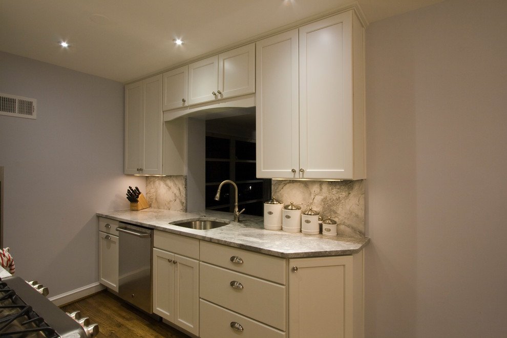 Example of a small transitional galley medium tone wood floor enclosed kitchen design in DC Metro with an undermount sink, stone slab backsplash, stainless steel appliances, recessed-panel cabinets, white cabinets, quartz countertops, gray backsplash and no island