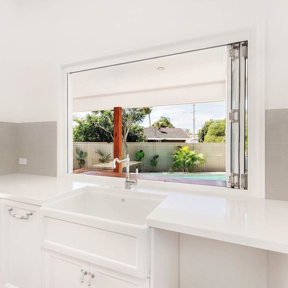 Design ideas for a large contemporary galley open plan kitchen in Gold Coast - Tweed with a farmhouse sink, shaker cabinets, white cabinets, quartz benchtops, beige splashback, subway tile splashback, stainless steel appliances, laminate floors, with island, grey floor and beige benchtop.