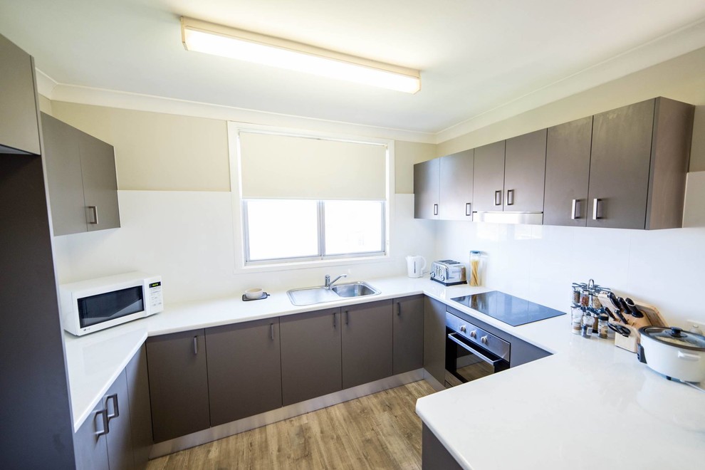 Photo of a mid-sized contemporary u-shaped eat-in kitchen in Newcastle - Maitland with a single-bowl sink, flat-panel cabinets, grey cabinets, laminate benchtops, white splashback, porcelain splashback, stainless steel appliances, medium hardwood floors, a peninsula, brown floor and white benchtop.