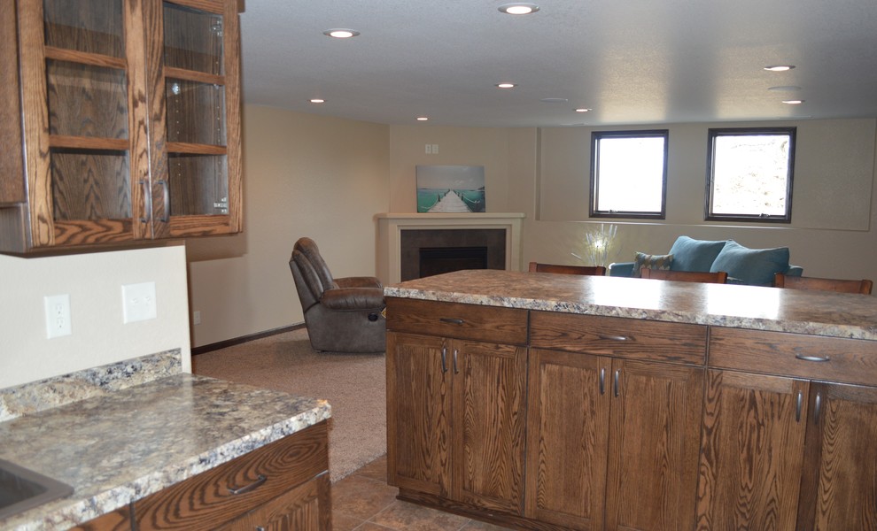 Mid-sized mountain style l-shaped laminate floor and beige floor eat-in kitchen photo with a drop-in sink, recessed-panel cabinets, dark wood cabinets, granite countertops, beige backsplash, ceramic backsplash, stainless steel appliances and an island