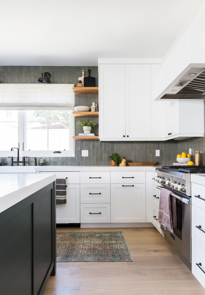 Design ideas for a mid-sized transitional l-shaped kitchen in San Diego with a farmhouse sink, shaker cabinets, white cabinets, solid surface benchtops, grey splashback, subway tile splashback, panelled appliances, light hardwood floors, with island and beige floor.