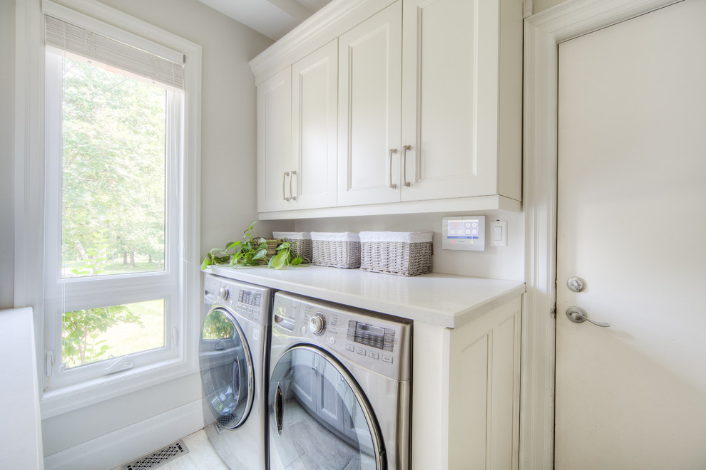 Photo of a mid-sized transitional galley dedicated laundry room in Toronto with an undermount sink, recessed-panel cabinets, white cabinets, limestone benchtops, beige walls, porcelain floors, a side-by-side washer and dryer, beige floor and white benchtop.