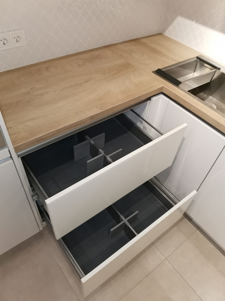 This is an example of a small contemporary l-shaped eat-in kitchen in Other with a drop-in sink, flat-panel cabinets, white cabinets, laminate benchtops, beige splashback, ceramic splashback, black appliances, porcelain floors, no island, beige floor and beige benchtop.