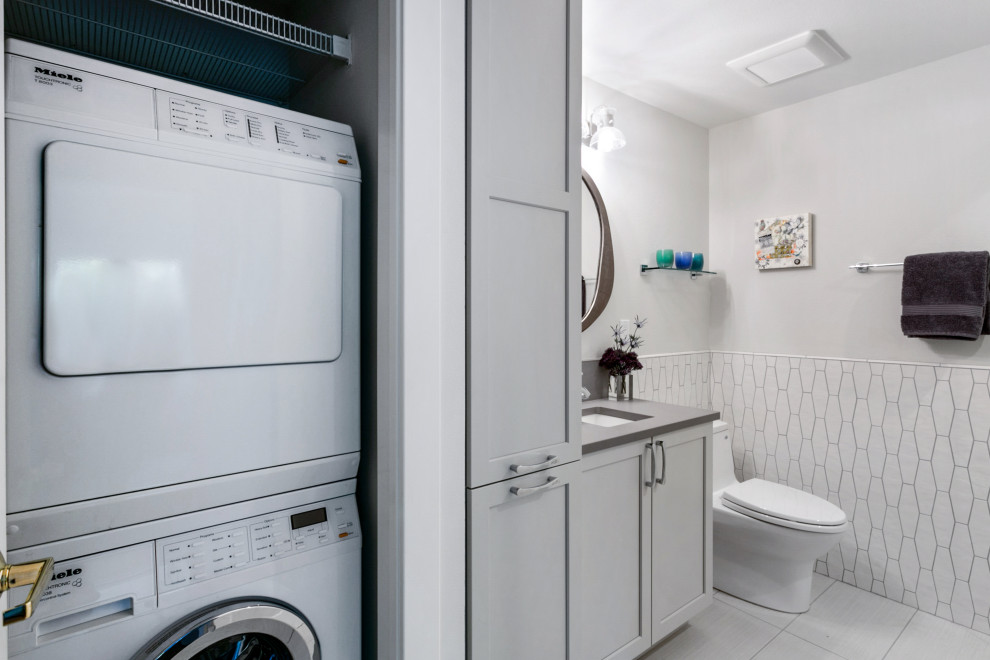 На фото: маленькая серо-белая ванная комната со стиральной машиной в стиле неоклассика (современная классика) с фасадами с утопленной филенкой, серыми фасадами, унитазом-моноблоком, белой плиткой, керамической плиткой, белыми стенами, полом из керамогранита, душевой кабиной, врезной раковиной, столешницей из искусственного кварца, серым полом, душем с распашными дверями, серой столешницей, тумбой под одну раковину, встроенной тумбой и душем в нише для на участке и в саду