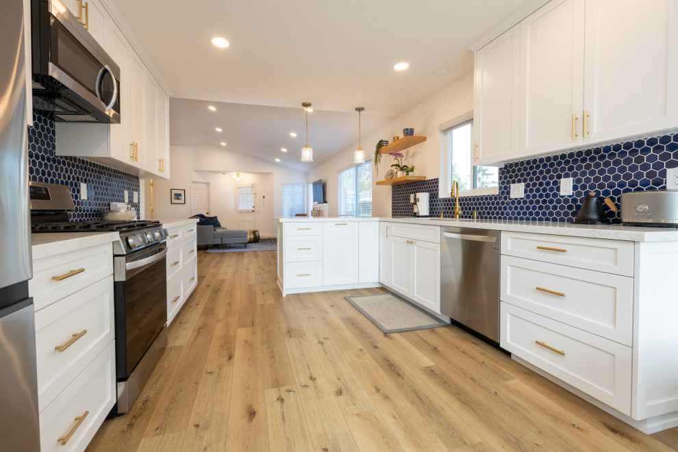 Bild på ett stort funkis vit vitt kök, med en undermonterad diskho, skåp i shakerstil, vita skåp, bänkskiva i kvarts, blått stänkskydd, stänkskydd i cementkakel, rostfria vitvaror, linoleumgolv och brunt golv