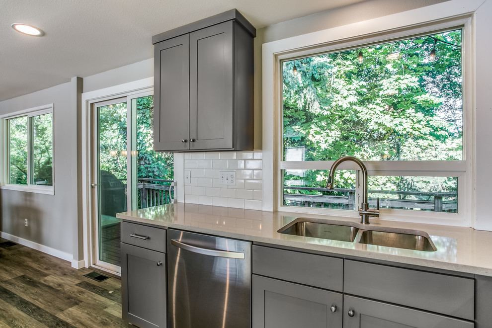 Mid-sized transitional l-shaped vinyl floor and brown floor eat-in kitchen photo with an undermount sink, shaker cabinets, gray cabinets, quartzite countertops, white backsplash, ceramic backsplash, stainless steel appliances and an island