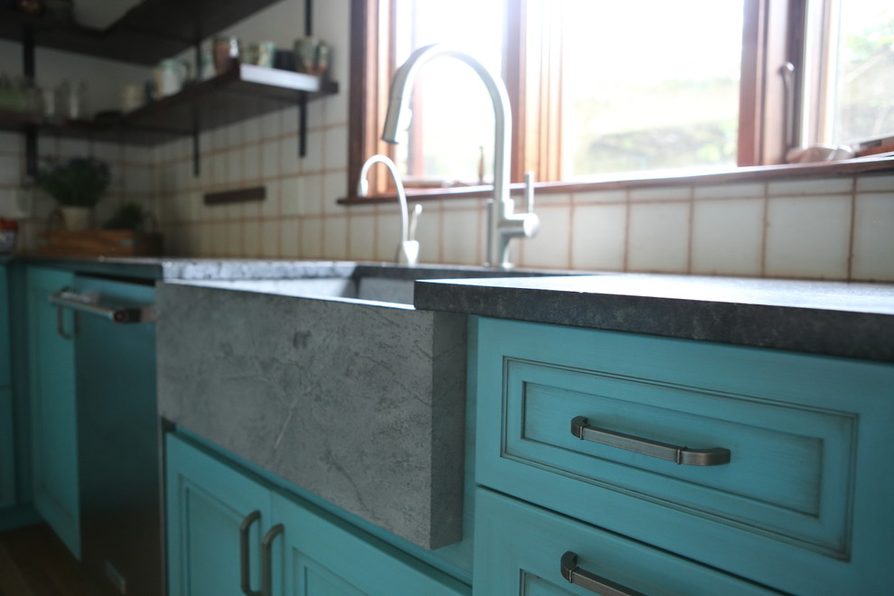 Mid-sized country l-shaped eat-in kitchen in Boston with a farmhouse sink, raised-panel cabinets, turquoise cabinets, soapstone benchtops, white splashback, ceramic splashback, stainless steel appliances, light hardwood floors, with island, brown floor and black benchtop.