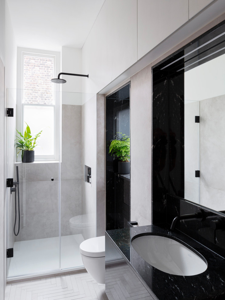 Mid-sized contemporary 3/4 bathroom in London with an alcove shower, a wall-mount toilet, gray tile, ceramic tile, ceramic floors, an undermount sink, granite benchtops, a hinged shower door, black benchtops, flat-panel cabinets, black cabinets and grey floor.