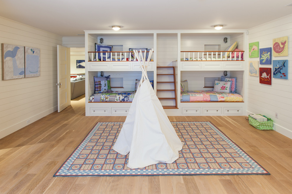 Photo of a large beach style gender-neutral kids' bedroom for kids 4-10 years old in Boston with white walls and medium hardwood floors.